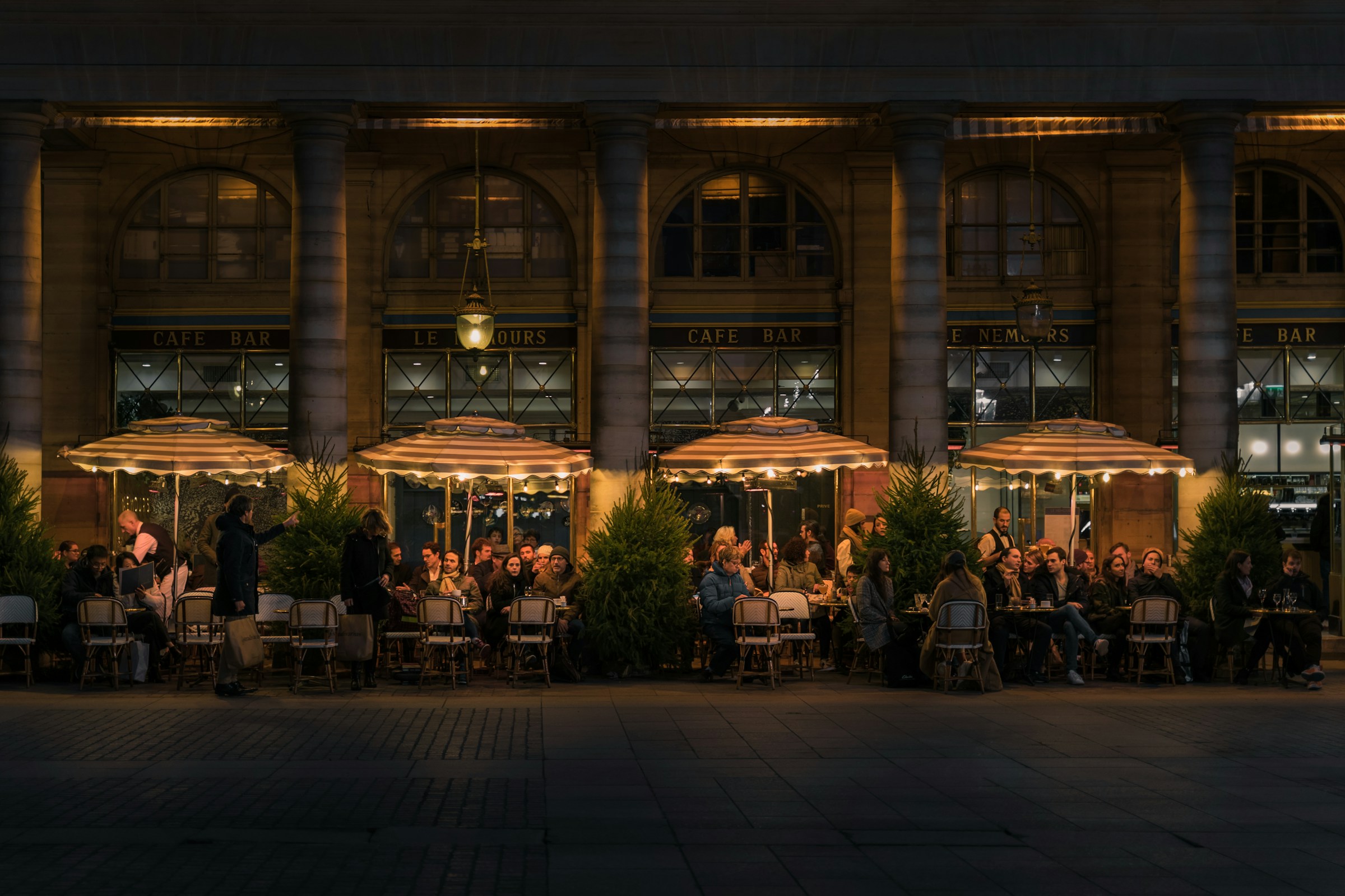 A busy street with people sat outside waiting for food