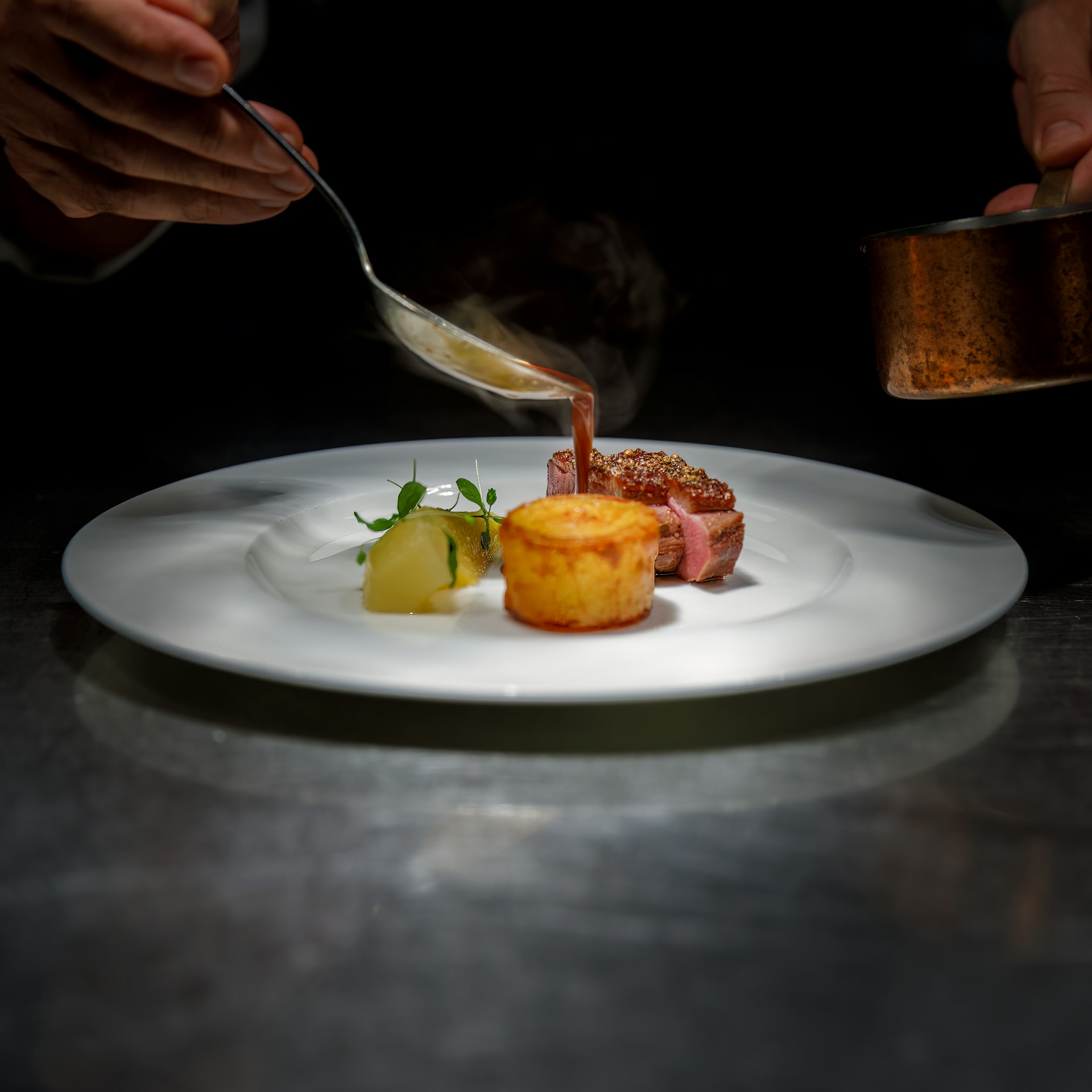 A chef drissling some sauce on a dish of a crispy potato fondant